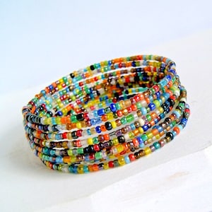May include: Multicolored beaded bracelet with a variety of colors, including red, orange, yellow, green, blue, and purple. The bracelet is made of small, round beads that are strung together on a thin wire.