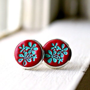 May include: A pair of red stud earrings with a silver setting. The earrings feature a turquoise floral design.