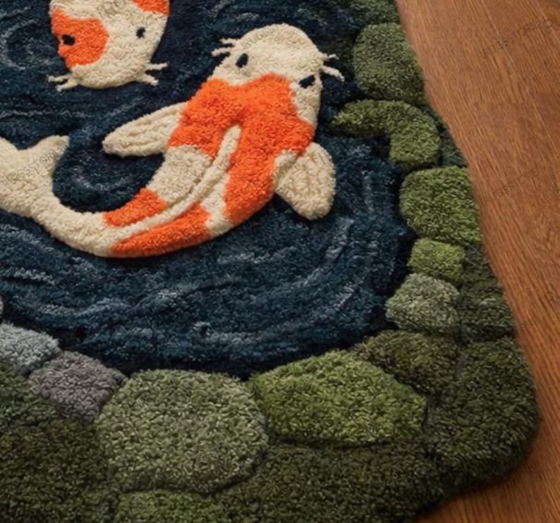 May include: A detailed rug featuring a koi fish design. The rug has a dark blue background with two koi fish in orange and white. Green and gray textured shapes represent plants and stones. The rug is made of a soft, textured material.