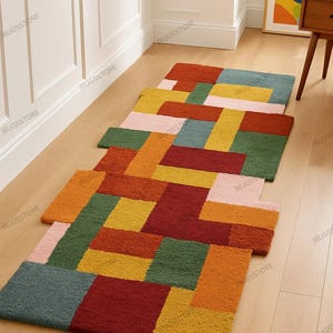 May include: Three colorful geometric rugs in shades of orange, red, green, yellow, pink, and blue are arranged on a light wood floor. The rugs have a textured, woven appearance and are rectangular in shape. The rugs are placed in a row.