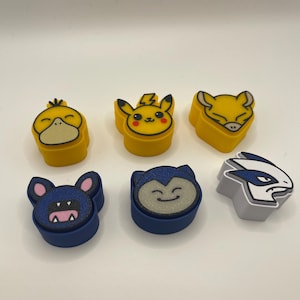 May include: Six colorful character-shaped erasers. The erasers feature designs of popular characters in yellow, blue, and gray. The characters include a duck, Pikachu, a fox, a bat, a Snorlax, and a Lugia.