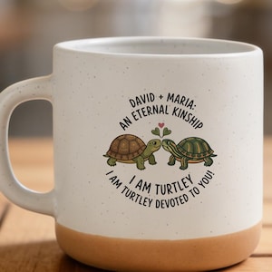 May include: A white ceramic mug with a speckled finish and a tan base. The front features an illustration of two turtles touching noses under a small heart, with the text: DAVID + MARIA: AN ETERNAL KINSHIP, I AM TURTLEY DEVOTED TO YOU!