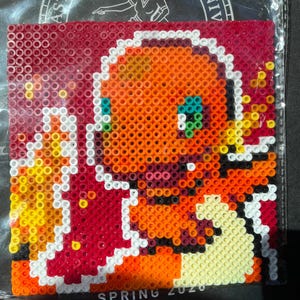 May include: A square pixel art piece featuring a Charmander design, created with colorful plastic beads. The artwork showcases a vibrant orange Charmander with blue eyes, a white outline, and a fiery tail. The background is a gradient of red and orange.