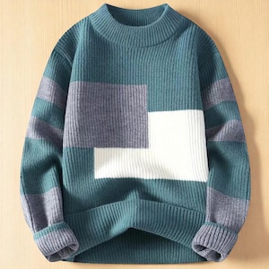 Peut inclure: Un pull à blocs de couleurs teal, gris et blanc avec une texture côtelée. Le pull présente un col ras du cou et des manches longues avec des poignets côtelés. Le design comprend un grand carré blanc et des rayures grises et teal.
