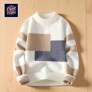 Może przedstawiać: Biały sweter z geometrycznym wzorem. Sweter ma wysoki dekolt, długie rękawy oraz prążkowany dół i mankiety. Wzór zawiera prostokątne bloki i paski w kolorze beżowym i szarym. W lewym górnym rogu znajduje się logo z napisem "Crystal Luxe Creation".