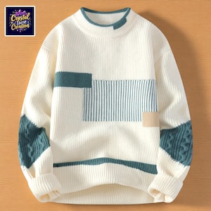 Puede incluir: Suéter color crema con detalles geométricos en verde azulado y beige. El suéter presenta una textura de punto acanalado, cuello redondo y mangas largas con detalles de punto trenzado verde azulado en los antebrazos. La esquina superior izquierda muestra un logo "Crystal Luxe Creation."