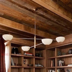 May include: A contemporary chandelier featuring five white, bowl-shaped shades. The light fitting has a gold-coloured central stem and horizontal arms. It hangs from a wooden ceiling in a room with bookshelves.