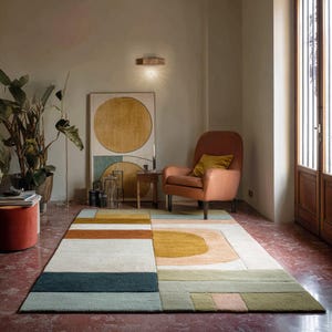 Könnte beinhalten: Ein rechteckiger Teppich mit geometrischem Design in Blau-, Grün-, Orange- und Cremetönen. Der Teppich liegt auf einem roten Boden, mit einem pfirsichfarbenen Sessel und Kunstwerken im Hintergrund. Der Raum ist gut beleuchtet.