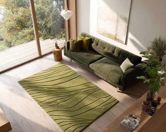 May include: A modern living room featuring a green sofa with several throw pillows, a green rug with a wave pattern, and a wooden coffee table. The room has large windows and a neutral color palette.