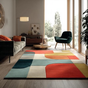 Op de afbeelding: Een modern vloerkleed met geometrische vormen in een woonkamer. Het kleed heeft rechthoekige en gebogen vormen in rood, oranje, geel, blauw en grijs. Het ligt op een houten vloer en voegt kleur toe.