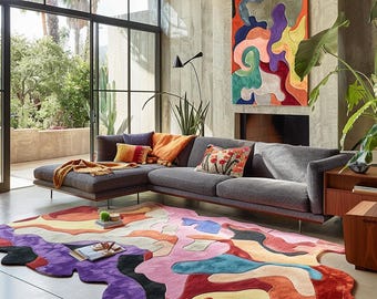 May include: A modern living room with a gray sectional sofa, colorful throw pillows, and a large abstract rug. The rug features a vibrant design with shades of purple, pink, orange, and yellow. A large painting with similar colors hangs on the wall.