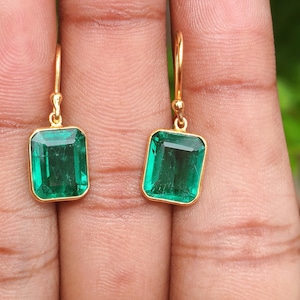 May include: A pair of gold-coloured earrings, each with a rectangular, emerald-green gemstone. The earrings have a simple design with a hook closure.