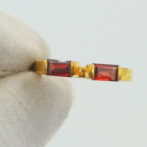 May include: Two gold rings, each with a rectangular, deep red gemstone. The rings have a simple, elegant design with a polished gold band and a bezel setting for the gemstones. The gemstones are approximately 0.6 cm in length.