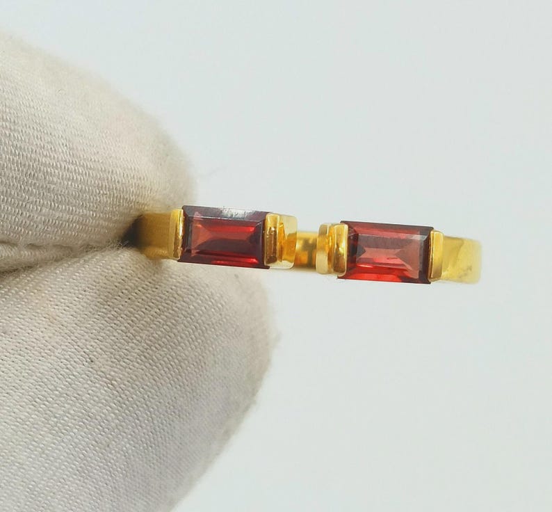 May include: Two gold rings, each with a rectangular, deep red gemstone. The rings have a simple, elegant design with a polished gold band and a bezel setting for the gemstones. The gemstones are approximately 0.6 cm in length.