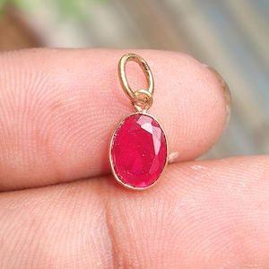 May include: A gold pendant featuring a bright red, oval-shaped gemstone. The stone is faceted, reflecting light. The pendant has a simple, elegant design, suitable for everyday wear or special occasions.