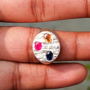 Peut inclure: Bague en argent avec une face ovale ornée d'une pierre rose vif, d'une pierre bleu foncé et d'une pierre orange. La bague comporte également de petites pierres d'accent claires.