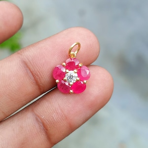 May include: A gold pendant in the shape of a flower. The pendant features six ruby petals surrounding a central diamond. The pendant is held by a gold loop.