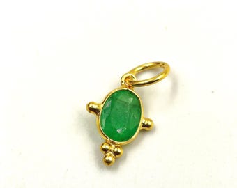 May include: A gold-colored pendant with a vibrant green, oval-shaped gemstone. The pendant has a small loop for hanging and decorative gold accents. The gemstone is the focal point, showcasing its rich color and cut.