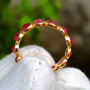 K&ouml;nnte beinhalten: Ein goldener Ring mit einer Reihe roter Edelsteine. Der Ring wird von einem wei&szlig;en Tuch gehalten. Die Edelsteine sind herzf&ouml;rmig und eng aneinander gesetzt, wodurch ein durchgehendes Farbband entsteht. Der Goldring ist zwischen den Steinen sichtbar.