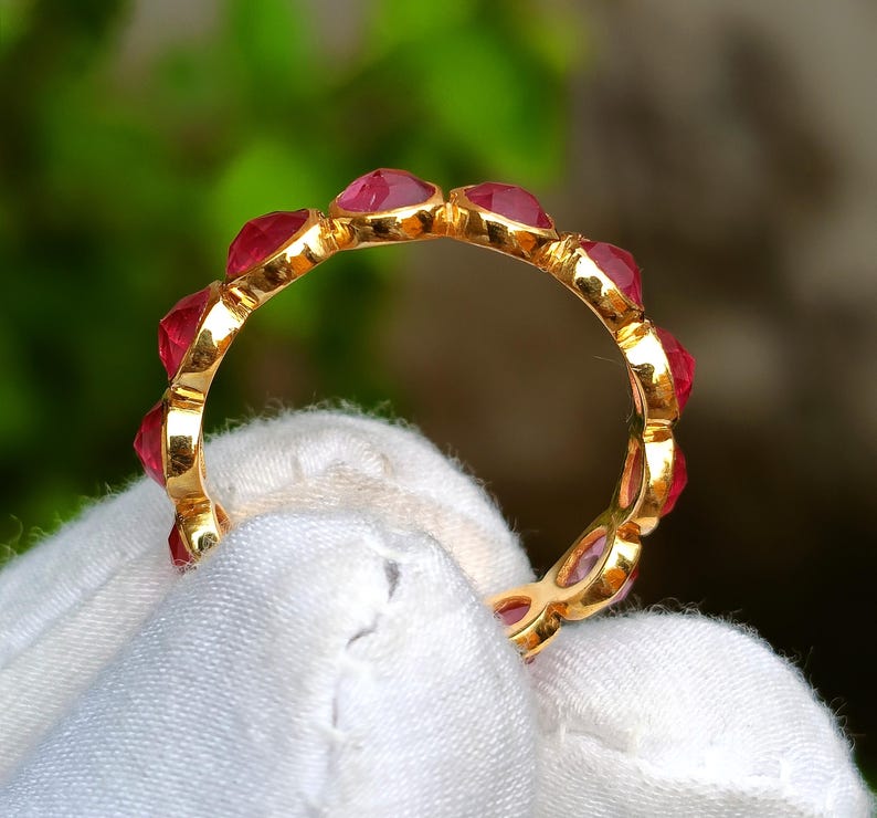 K&ouml;nnte beinhalten: Ein goldener Ring mit einer Reihe roter Edelsteine. Der Ring wird von einem wei&szlig;en Tuch gehalten. Die Edelsteine sind herzf&ouml;rmig und eng aneinander gesetzt, wodurch ein durchgehendes Farbband entsteht. Der Goldring ist zwischen den Steinen sichtbar.