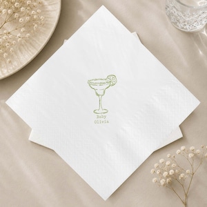 Könnte beinhalten: Eine quadratische weiße Papierserviette mit einer grünen Strichzeichnung eines Margaritaglases mit Limettenscheibe. Unter dem Glas steht der Text Baby Olivia in einer einfachen grünen Schrift. Die Serviette hat einen geprägten Rand.