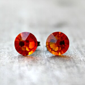 Puede incluir: Un par de pendientes de botón de cristal naranja. Los pendientes son redondos y tienen un diseño facetado.