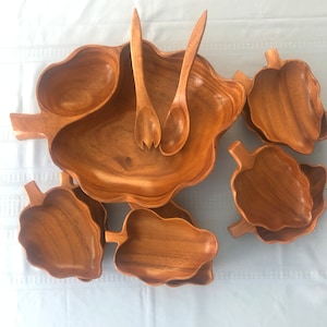 May include: A wooden serving set with a large, leaf-shaped bowl and six smaller bowls. The set also includes two wooden serving spoons.