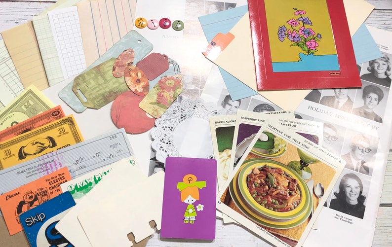 May include: A collection of vintage ephemera, including paper scraps, cards, and a small purple notebook with a girl illustration. The items are arranged on a wooden surface.