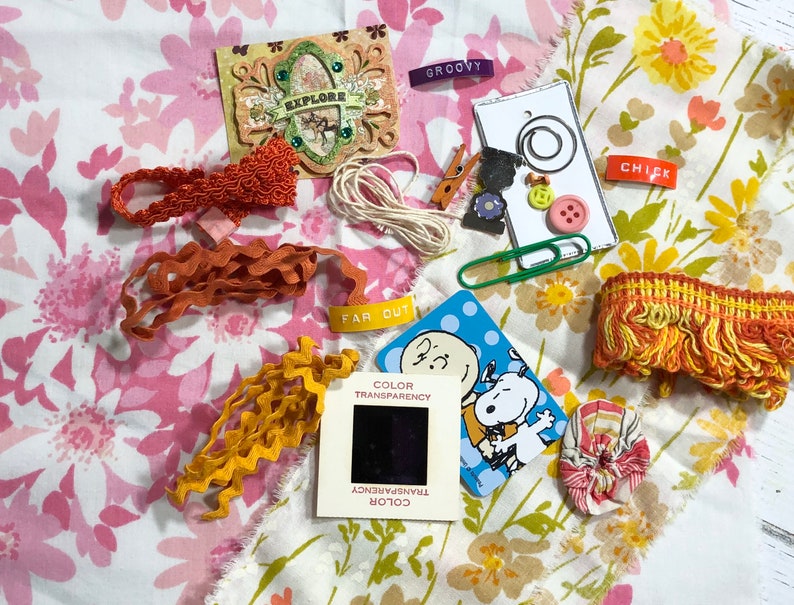 May include: A collection of craft supplies including fabric scraps, ribbon, trim, buttons, and a vintage slide. The fabric scraps feature floral patterns in pink, yellow, and orange. The ribbon is orange and yellow. The trim is orange and yellow. The buttons are red, yellow, and blue. The slide is black and white and features a cartoon image of Snoopy. The text "FAR OUT" and "COLOR TRANSPARENCY" are visible on the slide.
