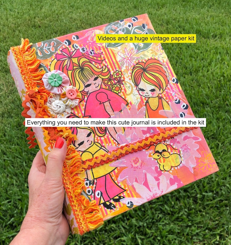 May include: A pink and orange journal with a vintage paper kit design. The cover features illustrations of girls and flowers. The text "Videos and a huge vintage paper kit" and "Everything you need to make this cute journal is included in the kit" is printed on the cover.