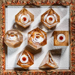 May include: A collection of polyhedral dice with a coffee theme, each featuring a miniature cup and saucer. The dice are encased in clear resin with gold numbering and are displayed within a decorative wooden frame.