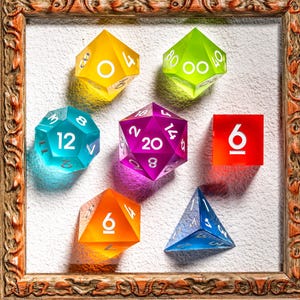 Puede incluir: Una colección de dados poliédricos coloridos de varias formas y tamaños, incluyendo un cuadrado, una pirámide y varios dados de múltiples caras. Los dados son en tonos amarillo, verde, azul, morado y naranja, con números blancos. Se muestran dentro de un marco de madera decorativo.