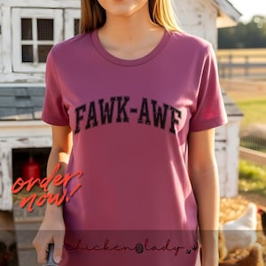 May include: A mauve-colored t-shirt with the text "FAWK-AWE" in black, arched lettering. The words "order now!" are in red script. The bottom of the shirt has the text "chickenlady" in a script font.