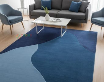 May include: A modern area rug in shades of blue, featuring a wave-like design. The rug has a light blue section that transitions into darker blues. The rug is placed in a living room with a gray sofa and blue chairs.