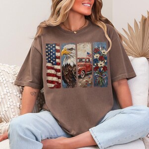 Puede incluir: Camiseta marr&oacute;n con un dise&ntilde;o patri&oacute;tico. El gr&aacute;fico incluye una bandera estadounidense, un &aacute;guila calva, una camioneta roja con una bandera y un ramo de flores. La camiseta es de corte holgado.