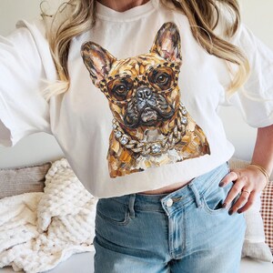 May include: White crew neck sweatshirt featuring a detailed illustration of a French Bulldog wearing leopard print glasses and a diamond chain. The dog's fur is a mix of brown and tan tones. The sweatshirt is a casual style.