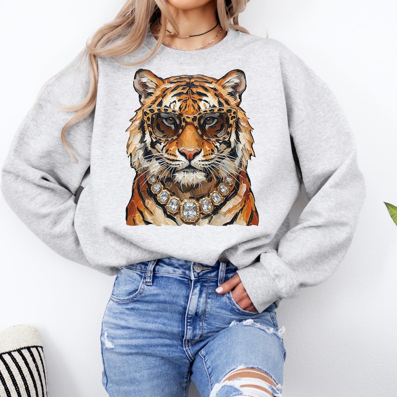 K&ouml;nnte beinhalten: Ein hellgraues Sweatshirt mit einer Aquarellillustration eines Tigers mit Sonnenbrille und Diamantkette. Der Tiger hat orange und schwarze Streifen. Das Sweatshirt ist ein l&auml;ssiger Stil.
