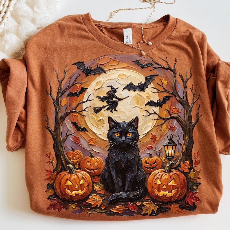 May include: A rust-colored t-shirt featuring a graphic print of a black cat sitting in front of a large yellow moon. The design includes carved jack-o'-lanterns, bare trees, flying bats, and a silhouette of a witch on a broomstick.