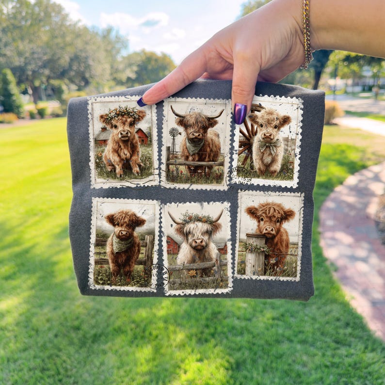 May include: Dark gray t-shirt featuring six postage stamp-style images of Highland cows. Each image showcases a different cow with various accessories, such as floral crowns and bandanas, set against a rural backdrop with barns and fences.