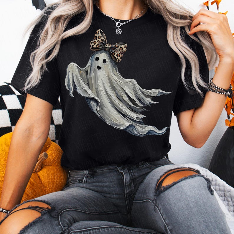 May include: Black t-shirt with a ghost illustration. The ghost is grey and wears a leopard print bow. The design is a fun take on Halloween themes.
