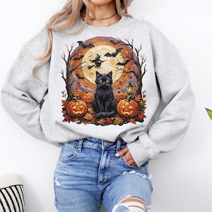 May include: A light gray crewneck sweatshirt featuring a graphic print of a black cat sitting among orange jack-o'-lanterns, autumn leaves, bare trees, flying bats, a witch on a broomstick, and a large full moon in the background.