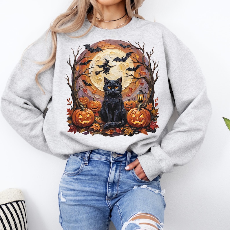 May include: A light gray crewneck sweatshirt featuring a graphic print of a black cat sitting among orange jack-o'-lanterns, autumn leaves, bare trees, flying bats, a witch on a broomstick, and a large full moon in the background.