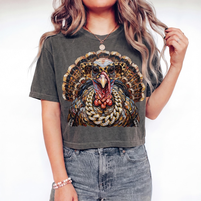 May include: A charcoal gray short-sleeve t-shirt featuring a graphic print of a turkey wearing leopard-print glasses and a thick gold chain. The turkey has detailed brown, tan, and orange feathers, a red wattle, and a prominent beak.