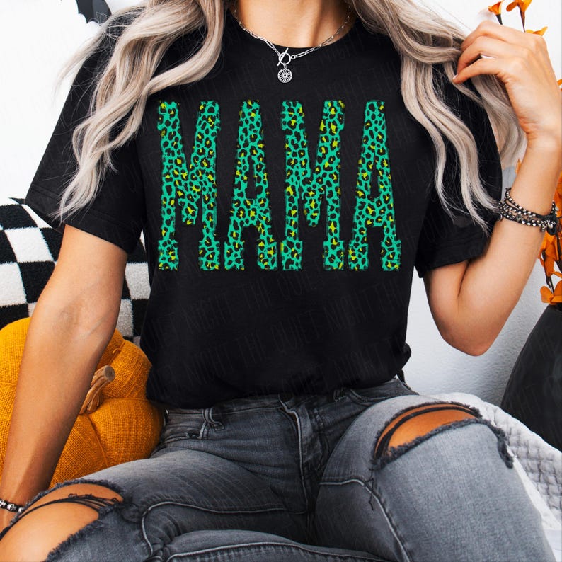 K&ouml;nnte beinhalten: Ein schwarzes T-Shirt mit kurzen &Auml;rmeln und dem Wort MAMA in einer fetten Blockschrift. Die Buchstaben sind mit einem leuchtend gr&uuml;nen und gelben Leopardenmuster gef&uuml;llt, was ein kontrastreiches Grafikdesign auf der Vorderseite des Shirts ergibt.