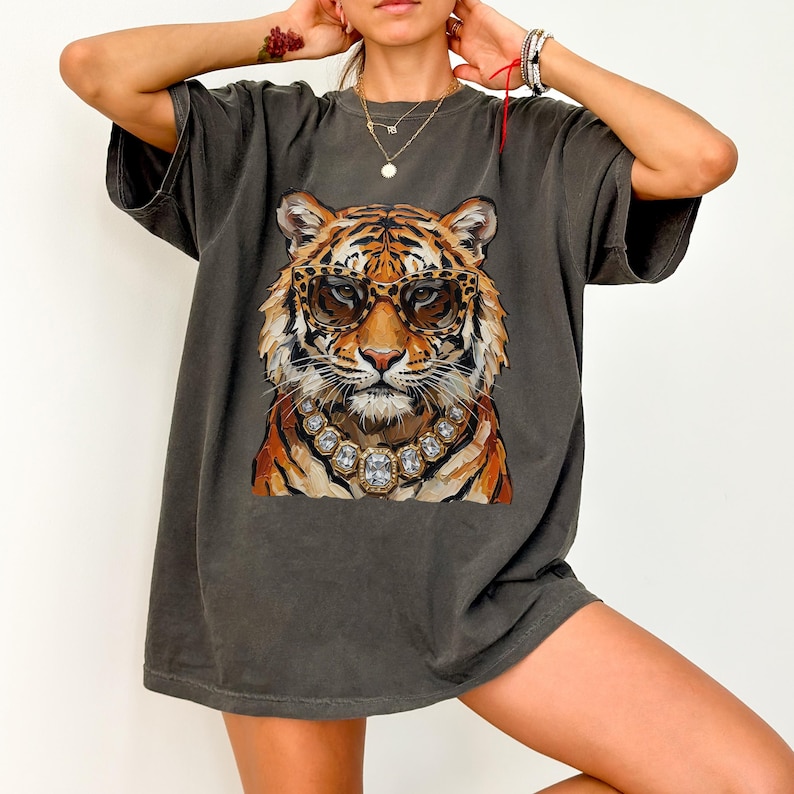 K&ouml;nnte beinhalten: Dunkelgraues T-Shirt mit einem Tiger, der eine Sonnenbrille und eine Diamantkette tr&auml;gt. Der Tiger hat orange und schwarze Streifen. Die Sonnenbrille hat ein Leopardenmuster. Das T-Shirt hat kurze &Auml;rmel.