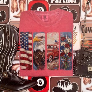Puede incluir: Una camiseta roja Comfort Colors con un dise&ntilde;o patri&oacute;tico. El dise&ntilde;o incluye una bandera estadounidense, un &aacute;guila calva, una camioneta roja y un ramo de flores. La camiseta es de cuello redondo y tiene una etiqueta que dice XL-TG-GG.