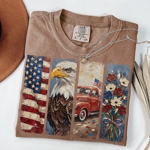 Puede incluir: Camiseta Comfort Colors marr&oacute;n con ilustraciones patri&oacute;ticas. El dise&ntilde;o incluye la bandera estadounidense, un &aacute;guila calva, una camioneta roja y un ramo de flores. Un collar plateado con un colgante est&aacute; sobre la camiseta.