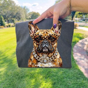 May include: A dark gray t-shirt featuring a detailed illustration of a French Bulldog wearing leopard print glasses and a diamond-studded chain. The dog's fur is painted in shades of brown and tan.