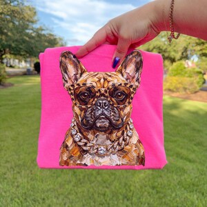 May include: A hot pink t-shirt featuring a detailed illustration of a French Bulldog wearing leopard print glasses and a diamond-studded chain. The dog's fur is a mix of brown and tan tones.