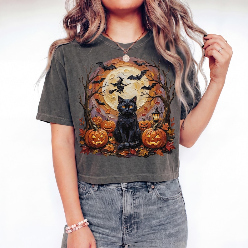 May include: A charcoal gray short-sleeve t-shirt featuring a graphic print of a black cat sitting among orange jack-o'-lanterns, autumn leaves, and bare trees. A full moon with a flying witch silhouette and bats is visible in the background.